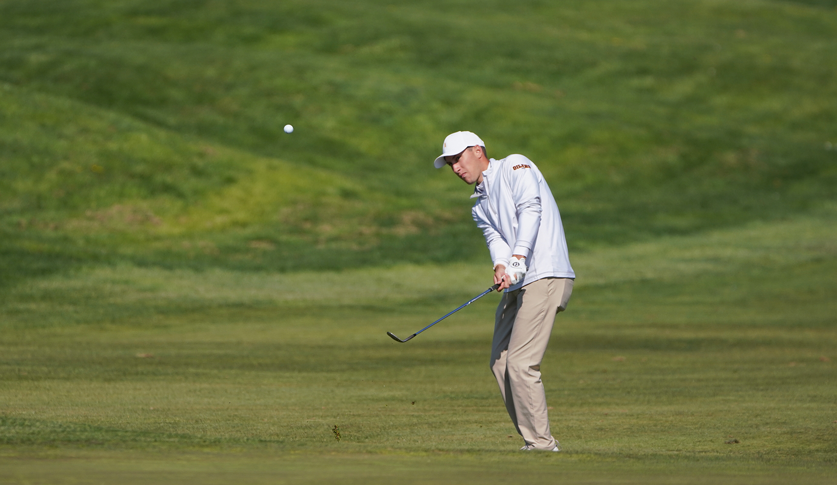 Male golfer chipping ball onto green from the fairway