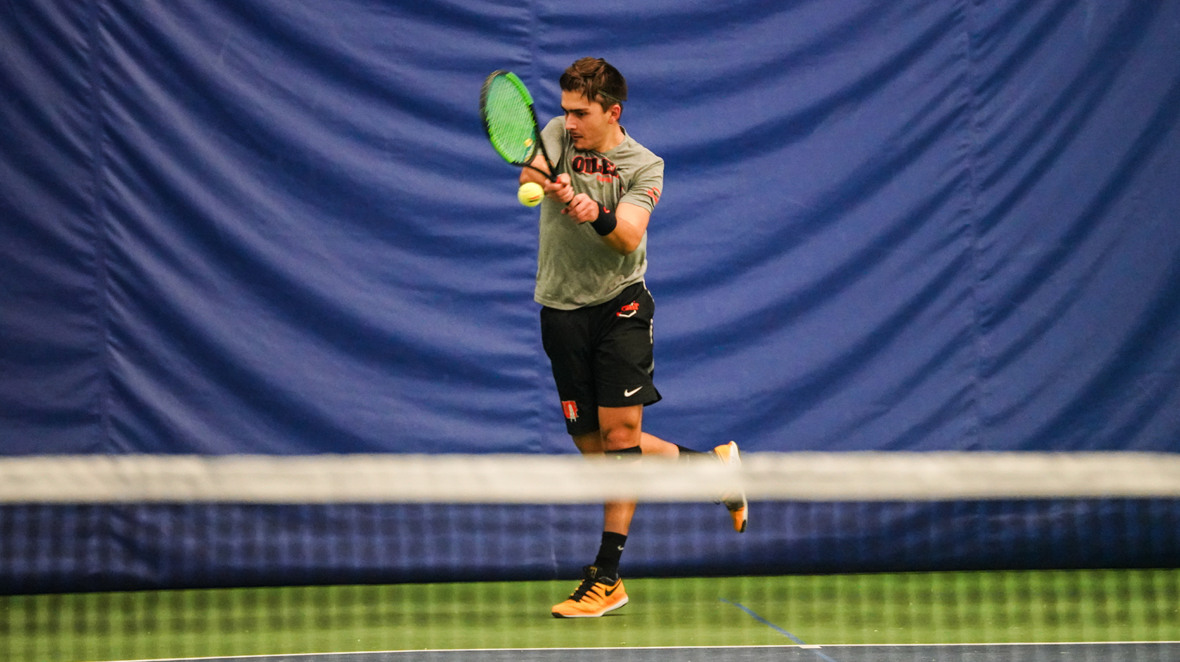 Men's tennis player in grey hitting a tennis ball indoors