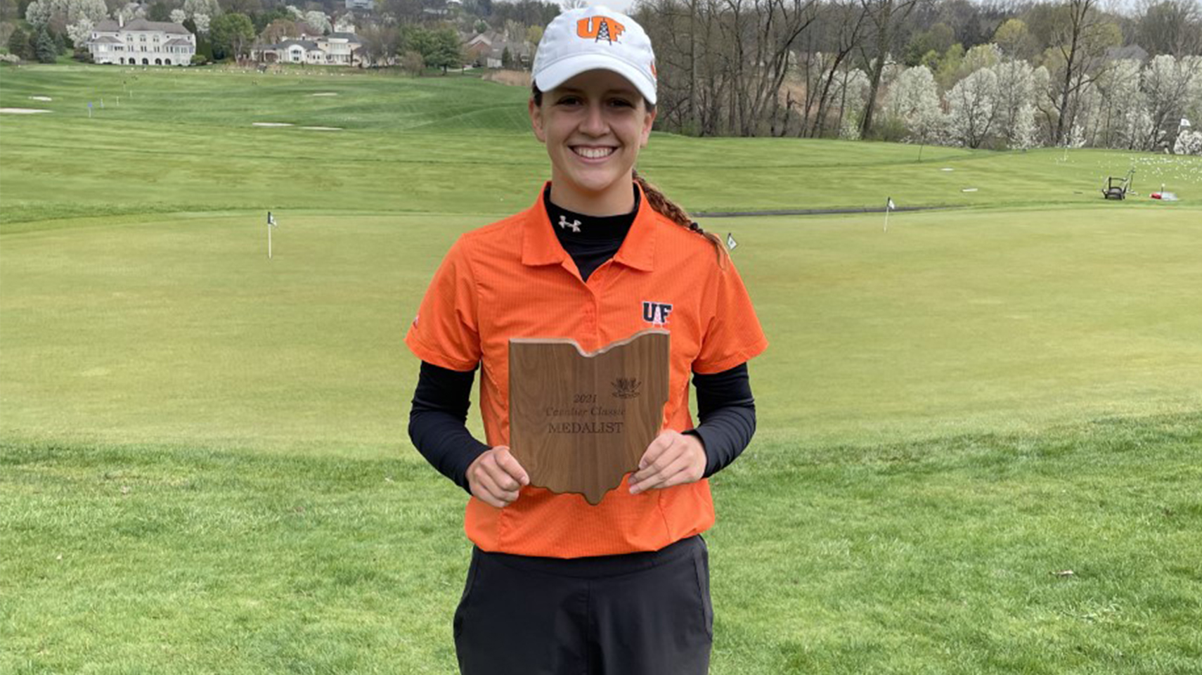 Women's golfer in orange holding a trophy