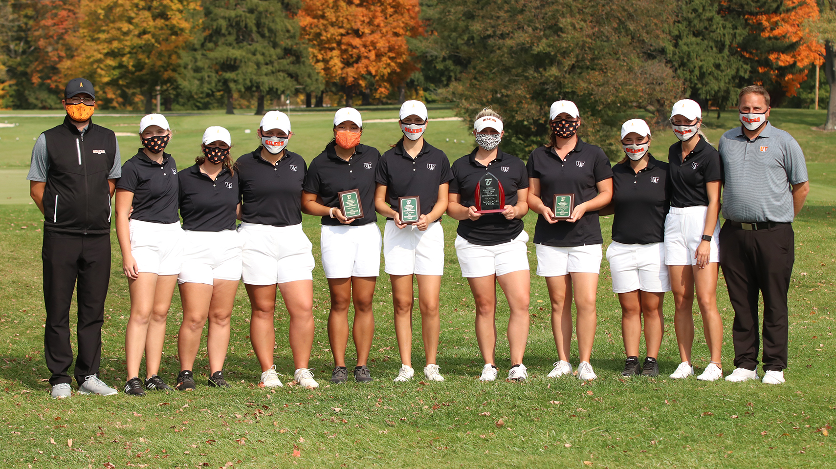 Women's golf team champions at Tiffin Fall Invitational. They are standing holding a trophy.