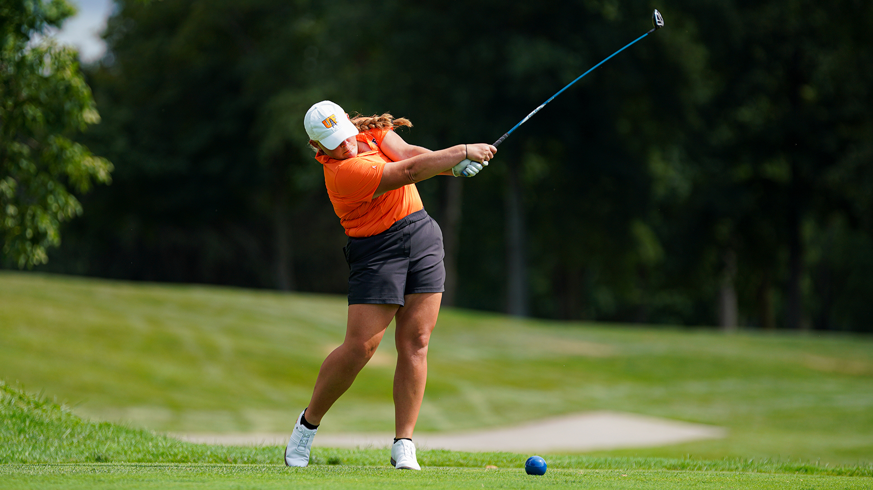 women's golf hitting driver off the tee in an orange shirt
