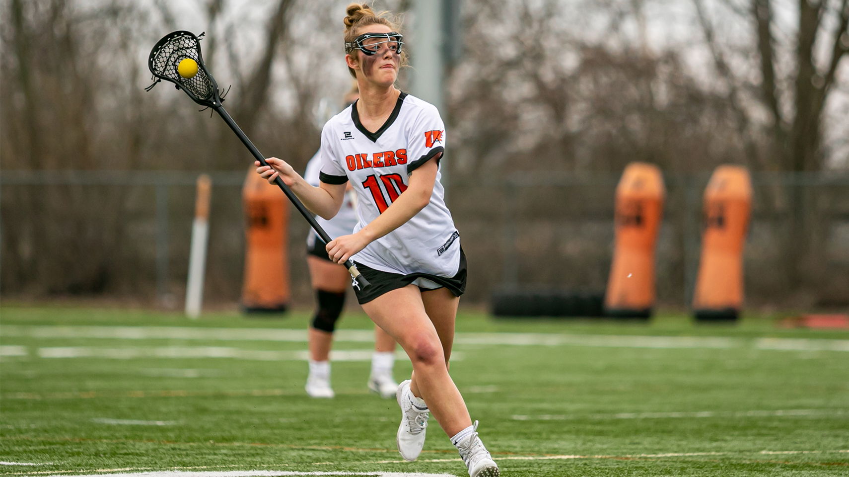 Women's lacrosse player running down the field with her ball in the stick