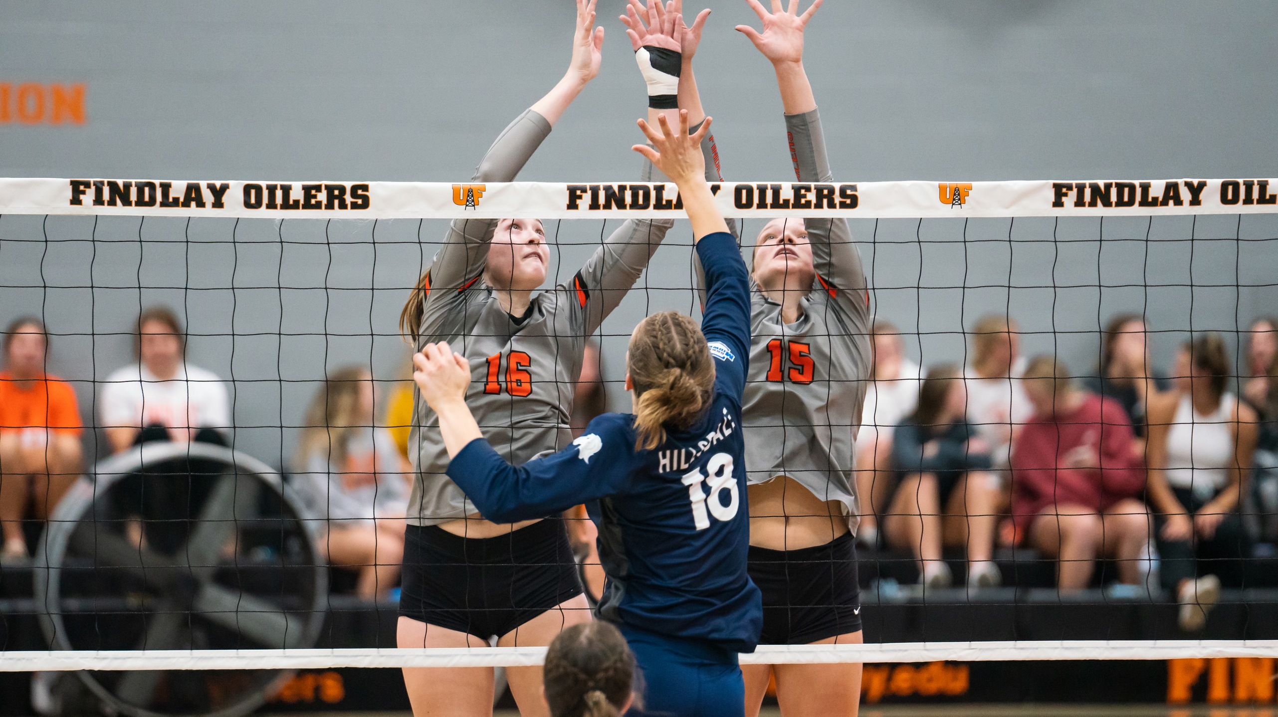 Two women in gray block the net in volleyball game. 