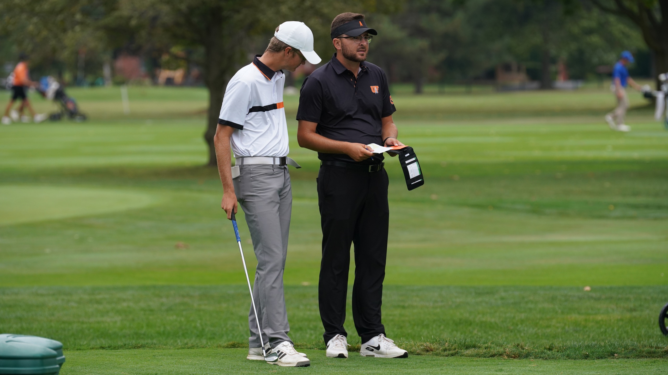 Coach and player look at yardage book on tee. 
