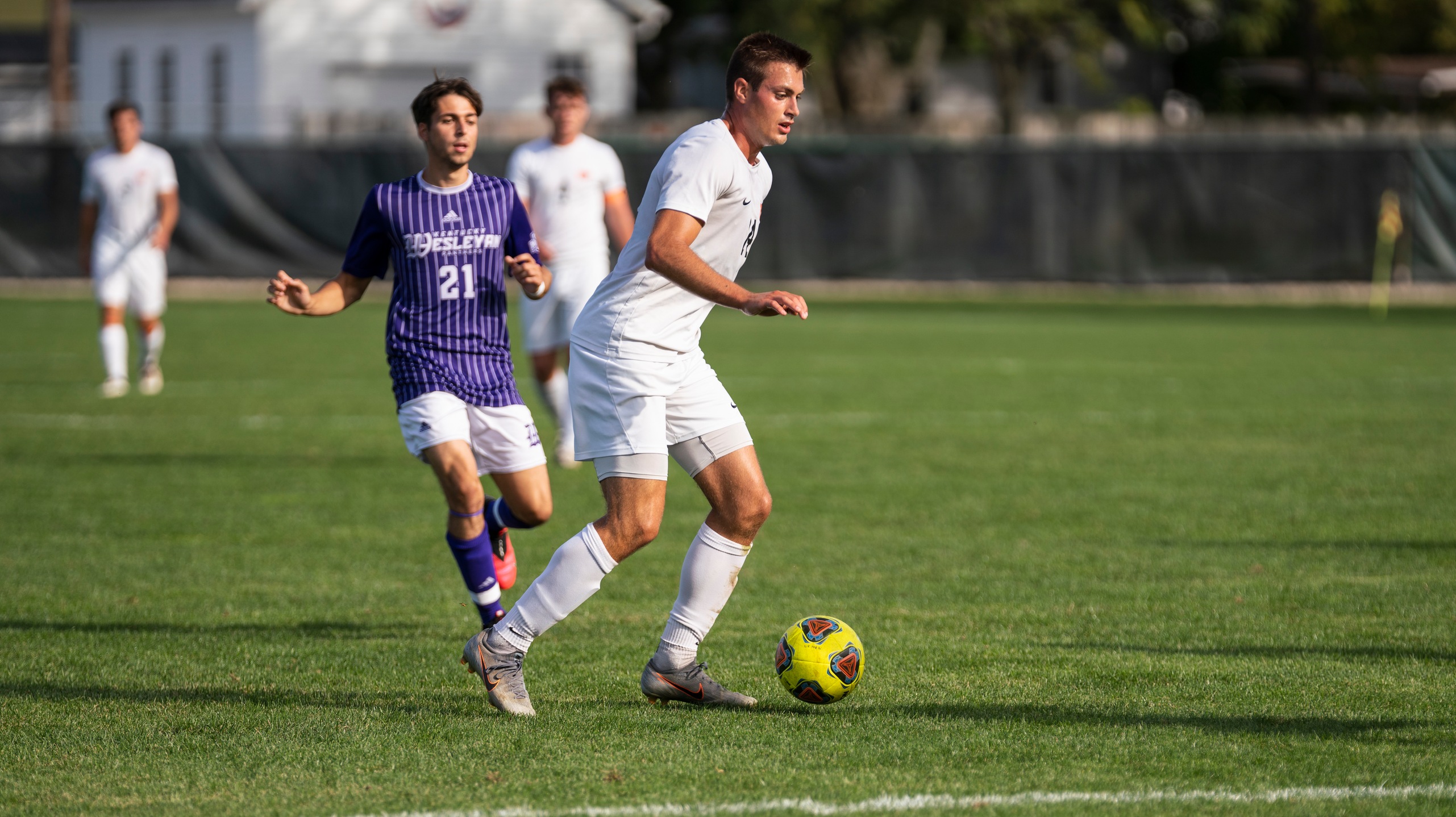 Soccer player in white controlling the ball with player in purple in the  background