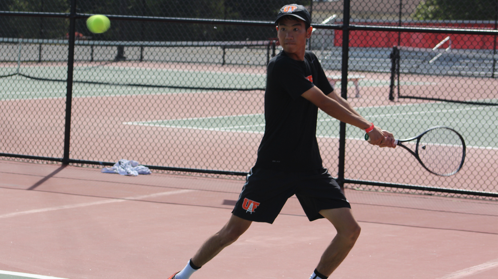 Men's tennis player in black returning serve.
