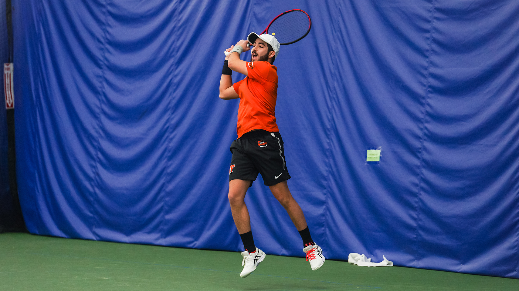 men's tennis player hitting the ball in front of blue drape