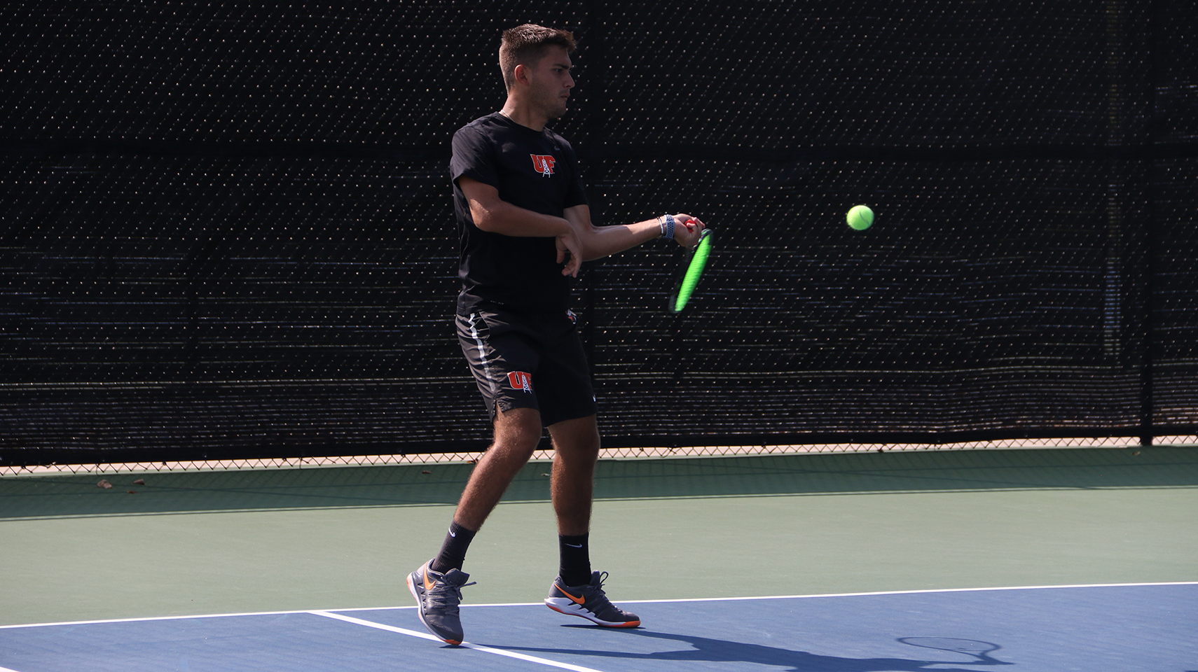 Men's tennis player hitting in a shadow on the court