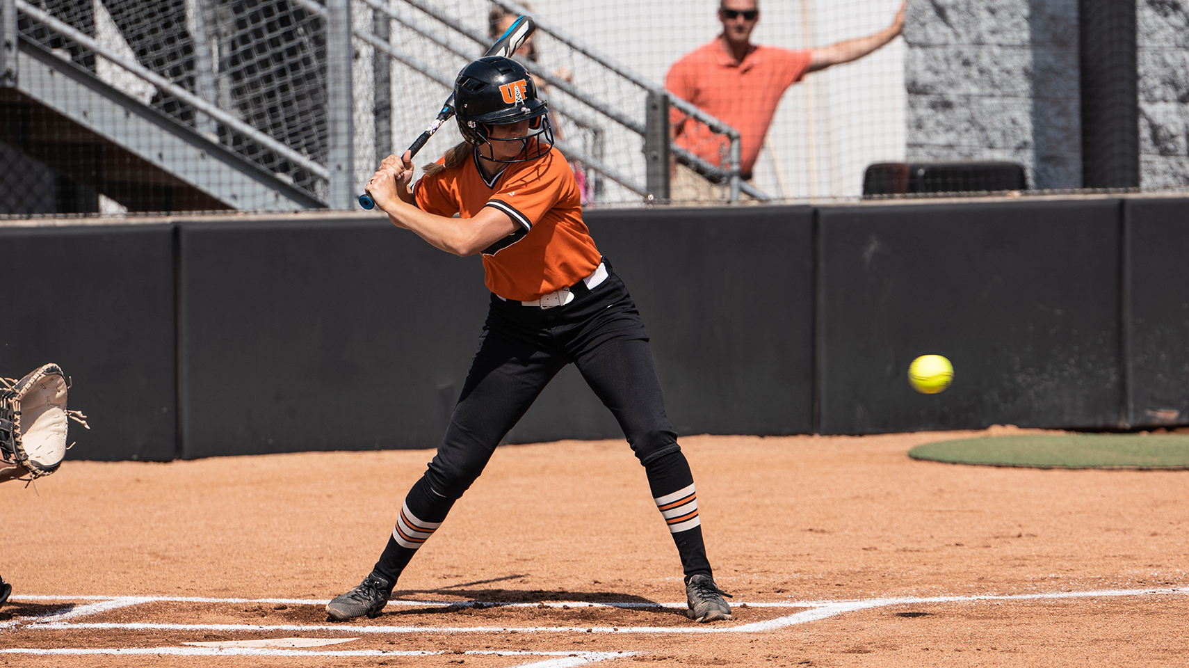 softball player in orange uniform taking a pitch at the plate