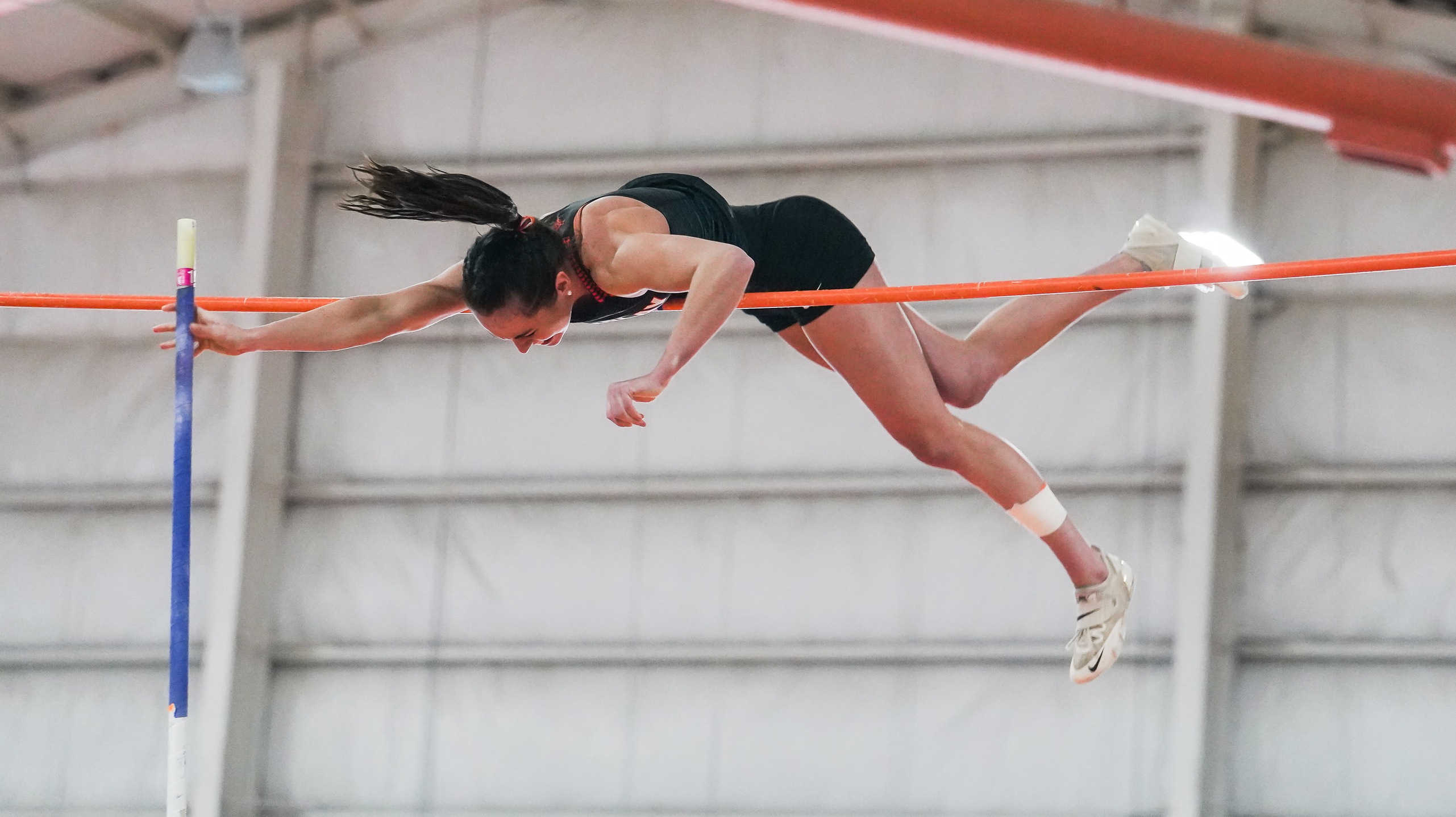 Girl in black soaring over a bar in sport of pole vault