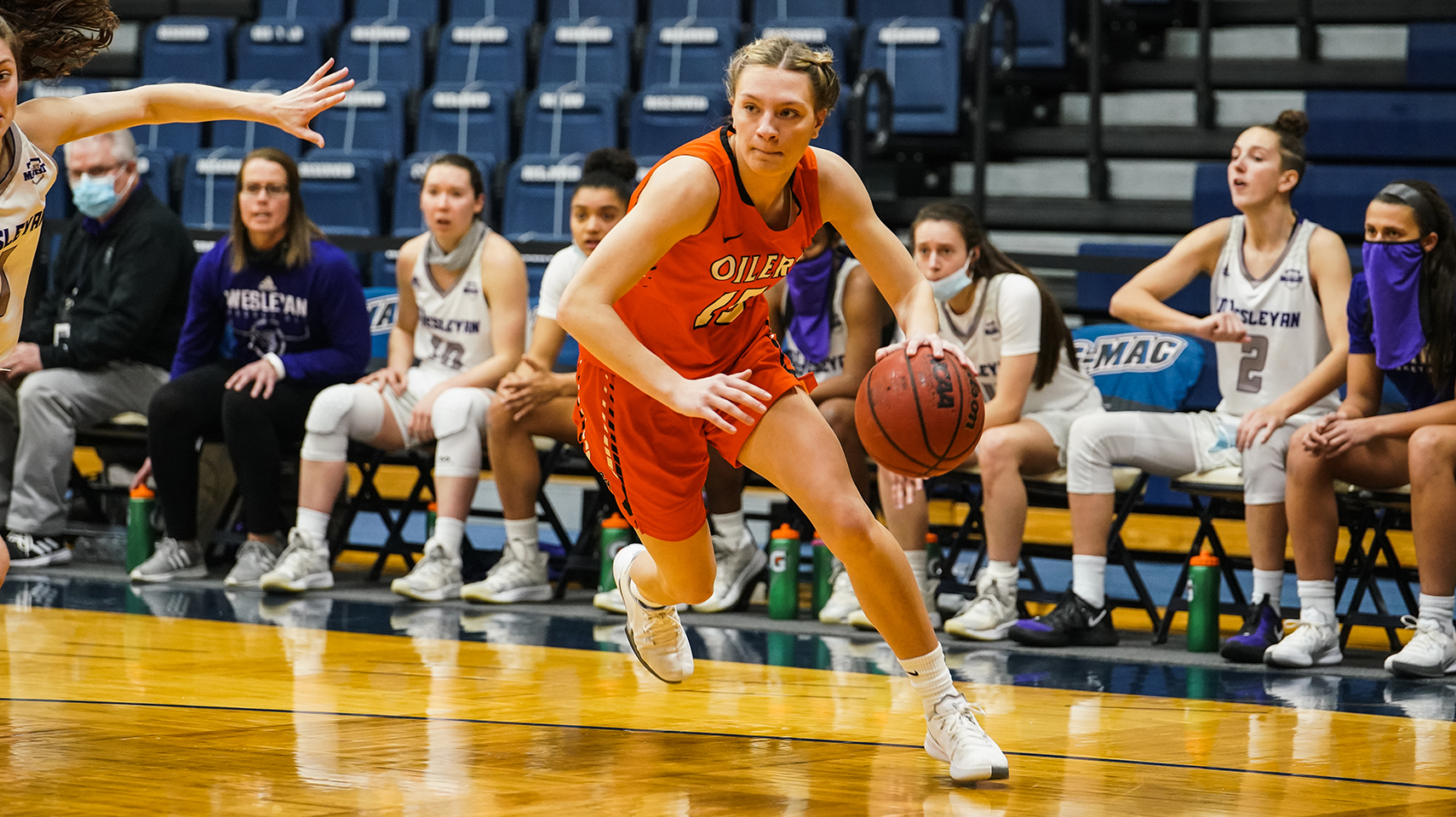 Women's basketball player in orange uniform driving baseline