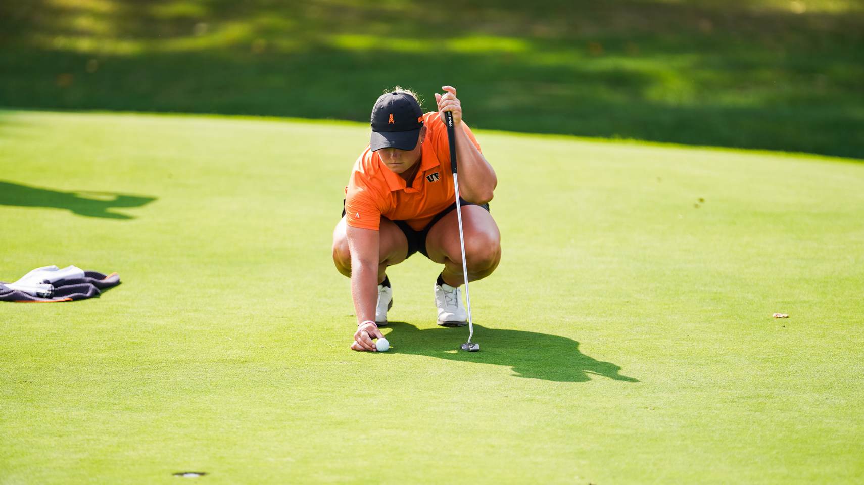 women's golfer in orange shirt placing the ball on the green for a putt