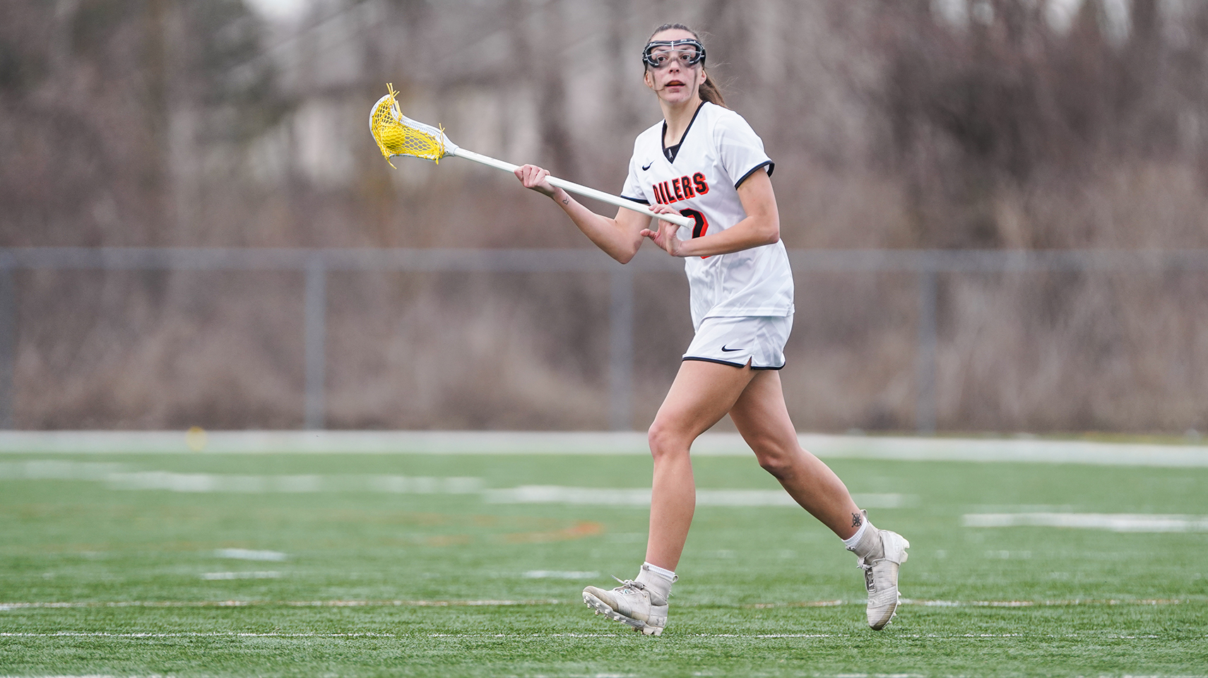 Women's lacrosse player in white uniform holding the ball.
