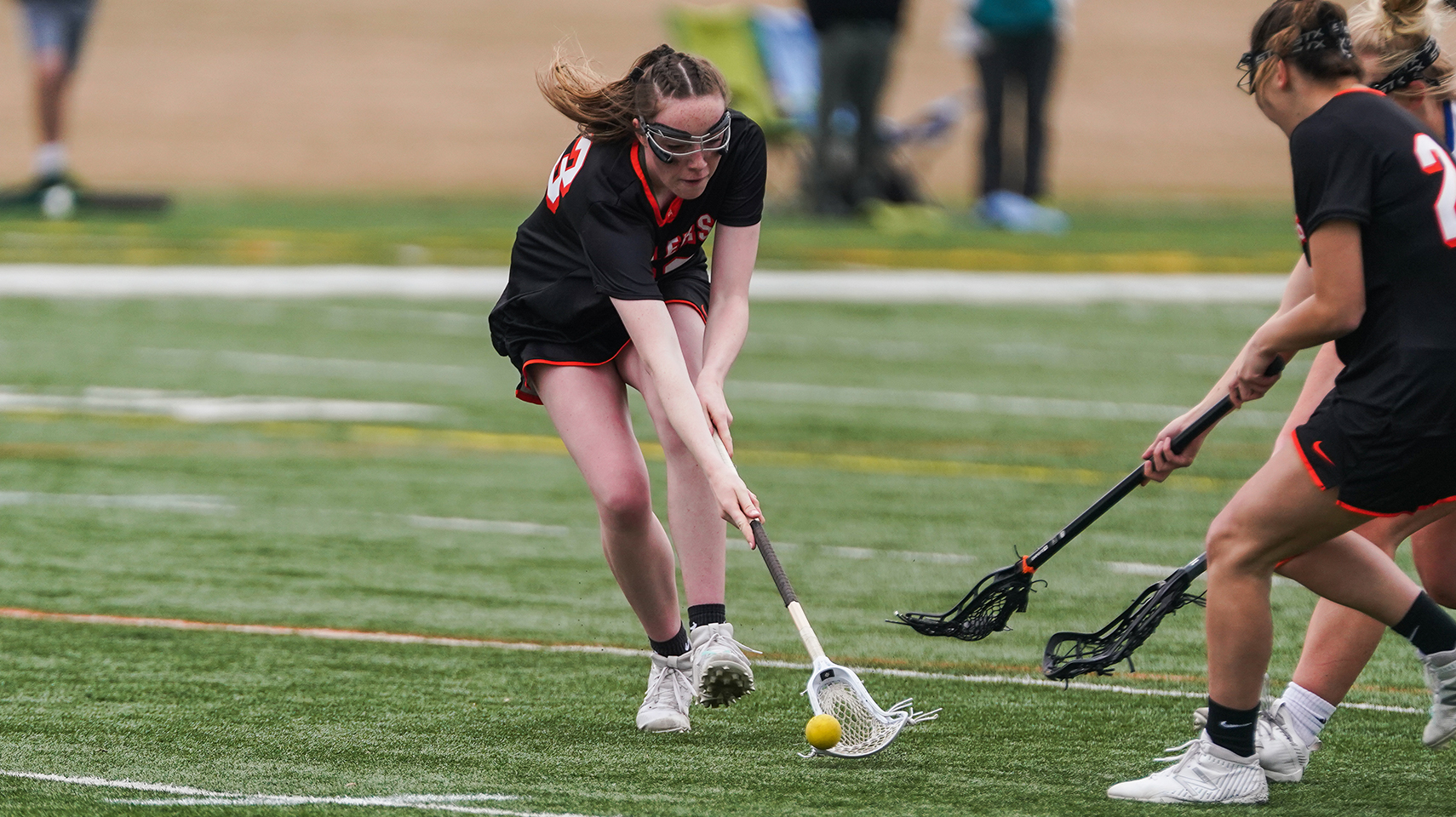Women's lacrosse player picking up a ball