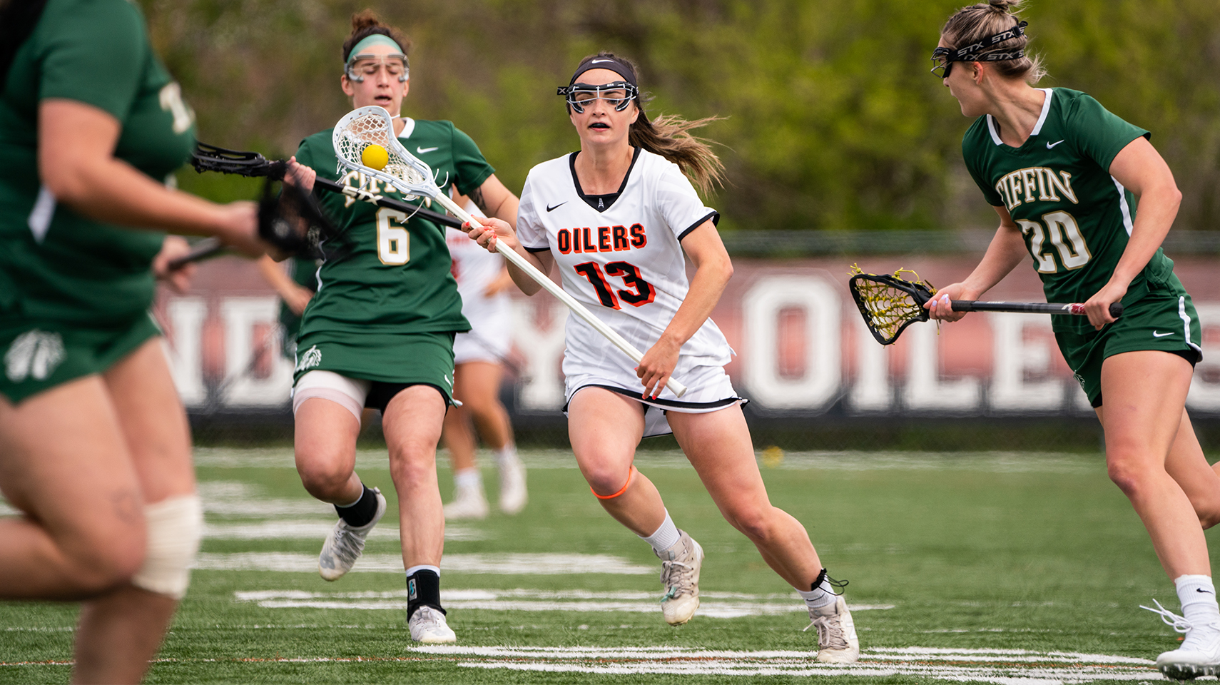 Women's lacrosse player in white between three defenders