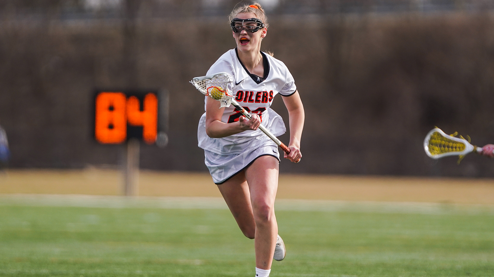 Women's lacrosse player in white running with the ball