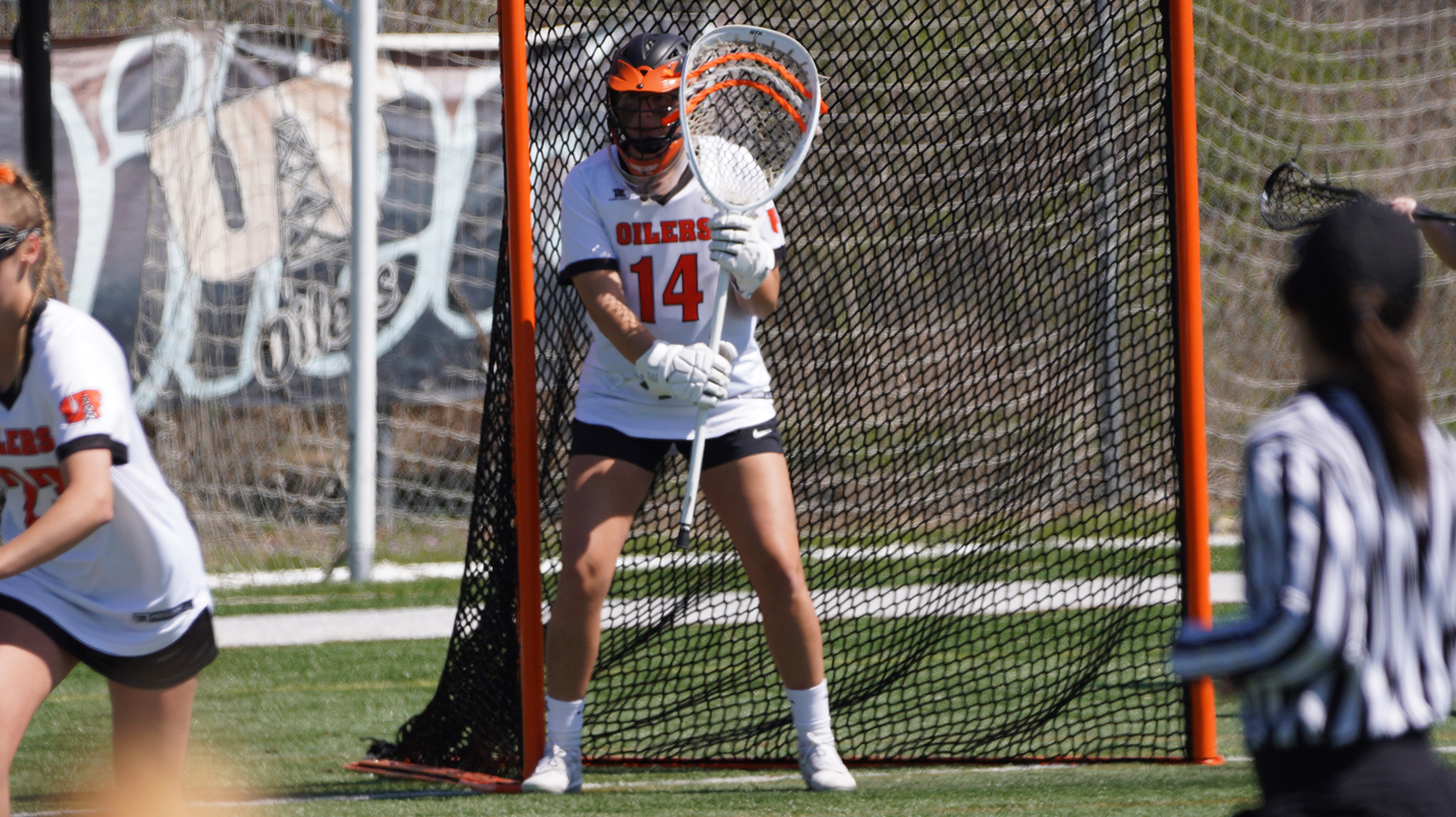Women's lacrosse goalie standing in front of the net with her stick up