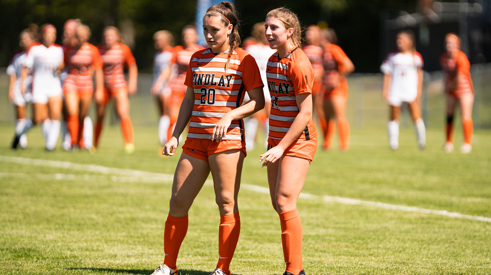 Two women's soccer players in orange jerseys talking on the field