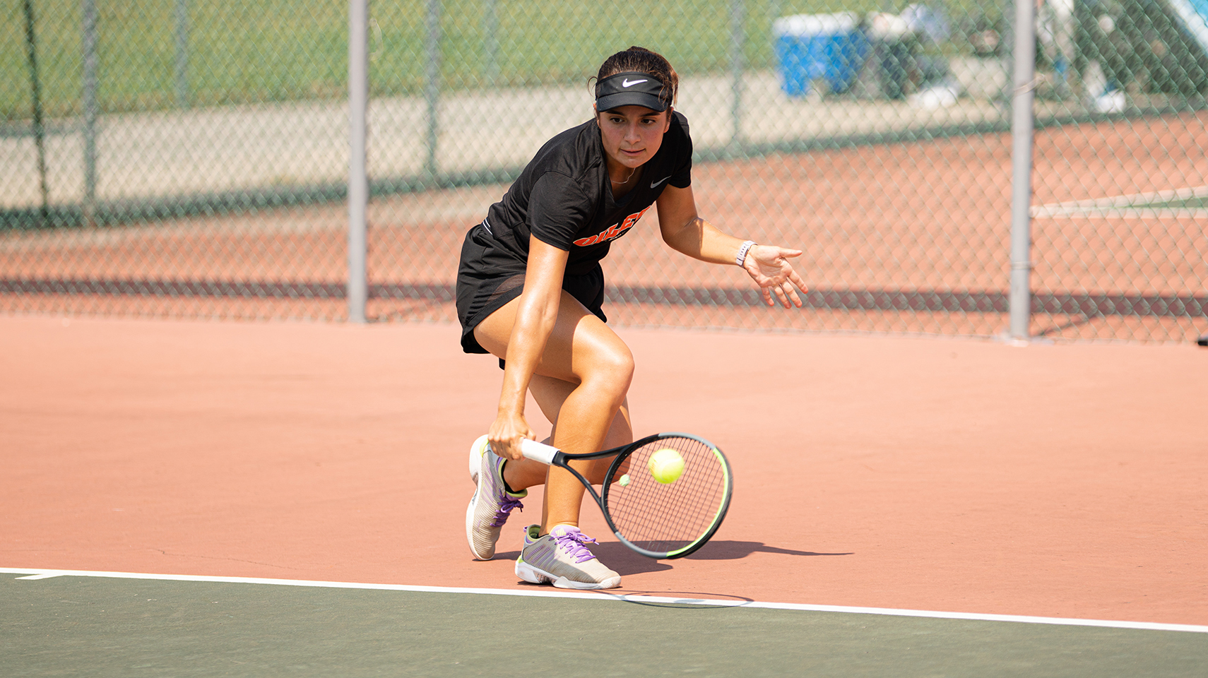 Women's tennis player reaching low to hit the ball