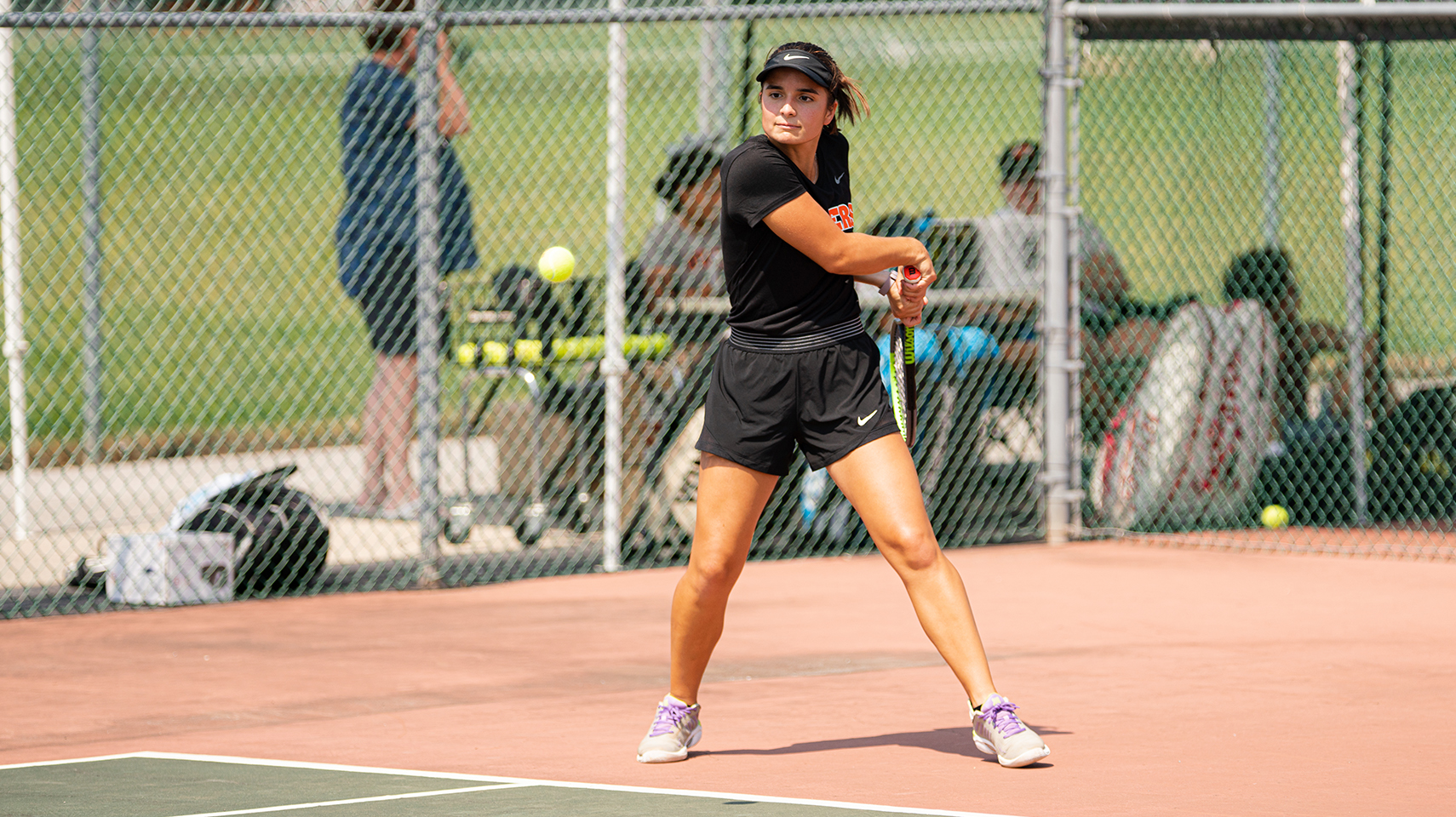 Women's tennis player in black uniform hitting the ball outside on a sunny day
