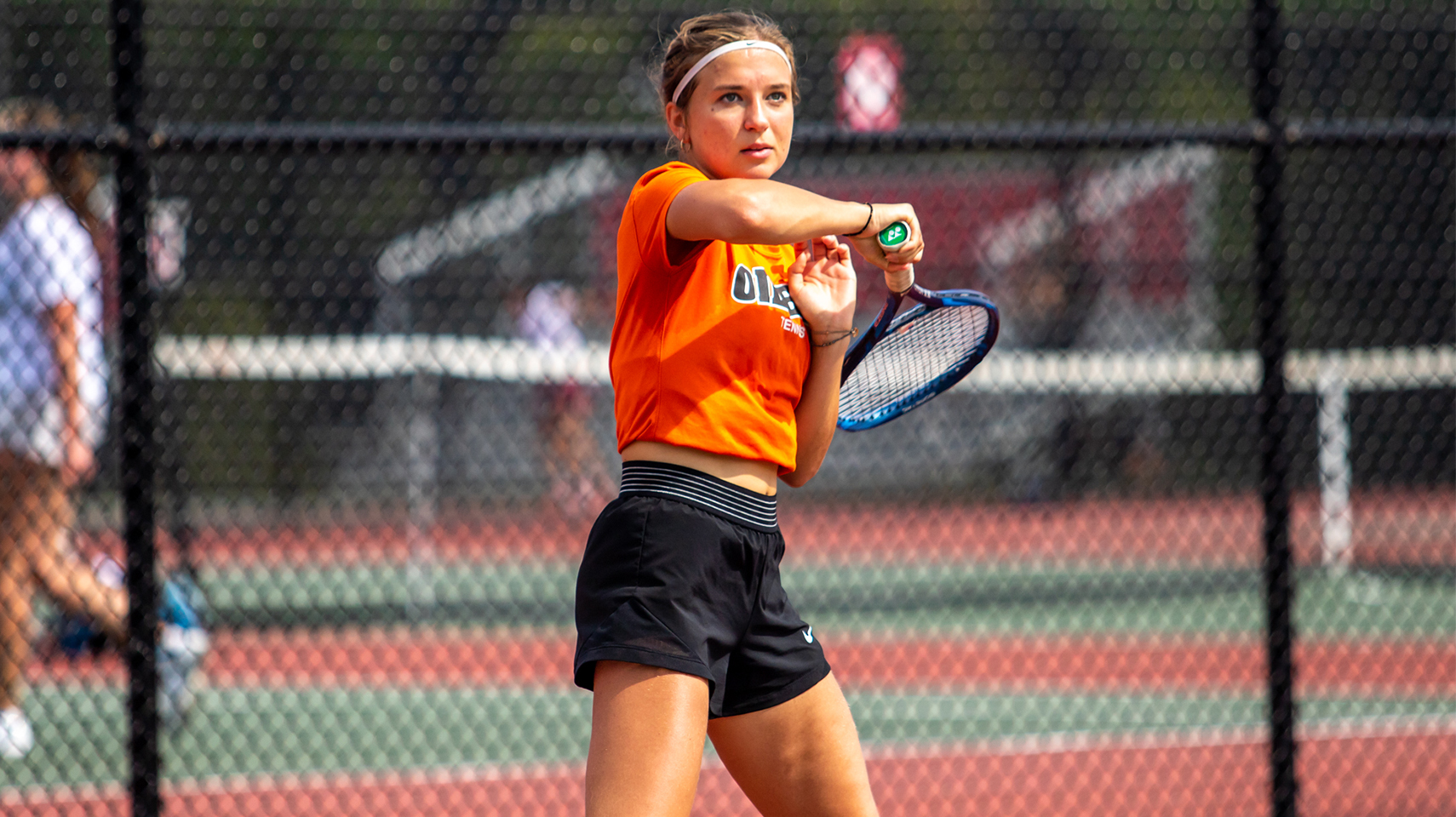 Women's tennis player in orange hitting the ball