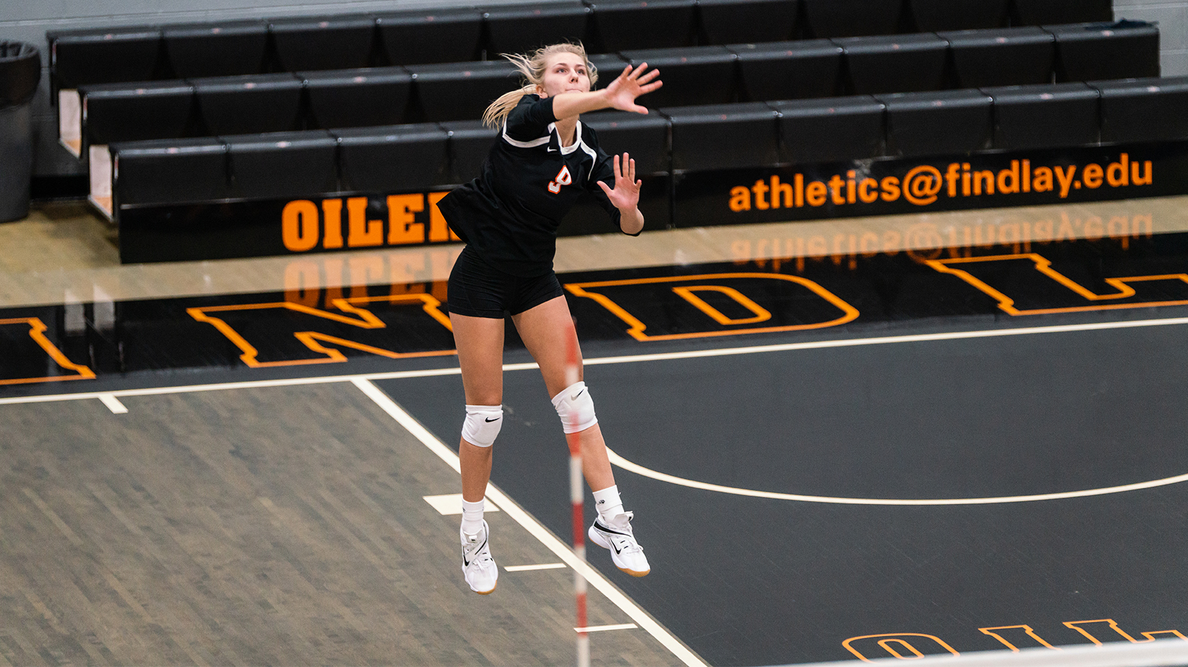 women's volleyball player in black jumping while serving