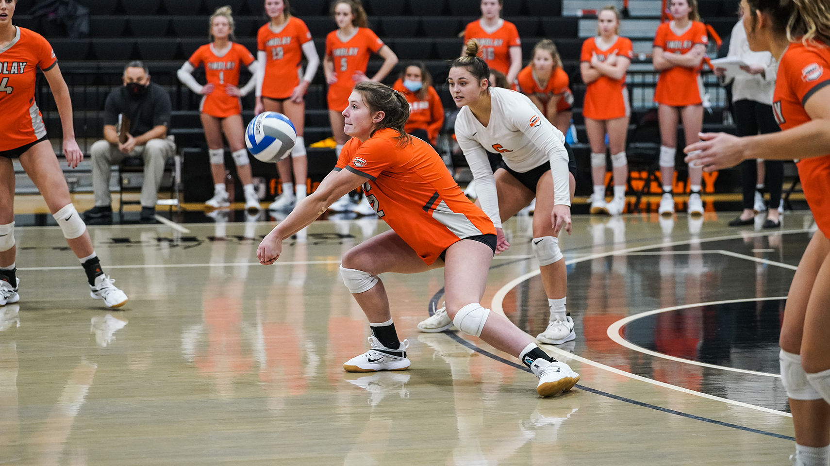 volleyball player in orange scraping the floor while digging the ball