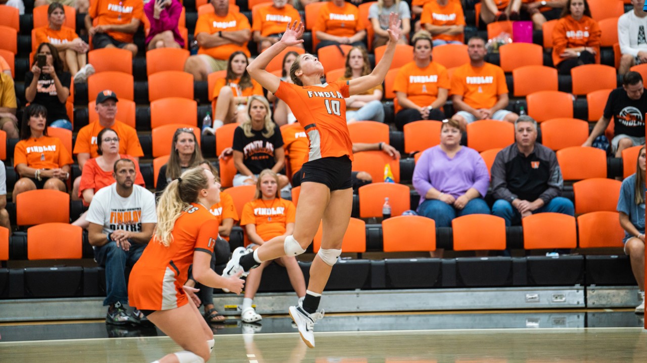 Volleyball girl in orange hits ball. 