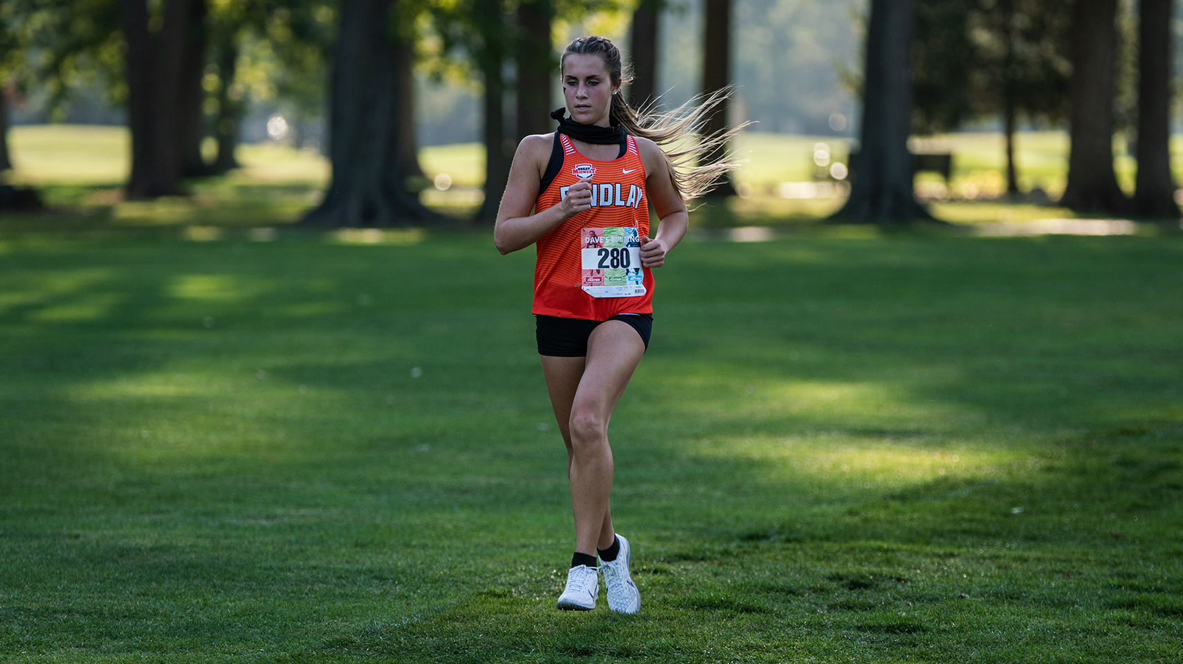 Women's cross country runner in orange racing through shadows