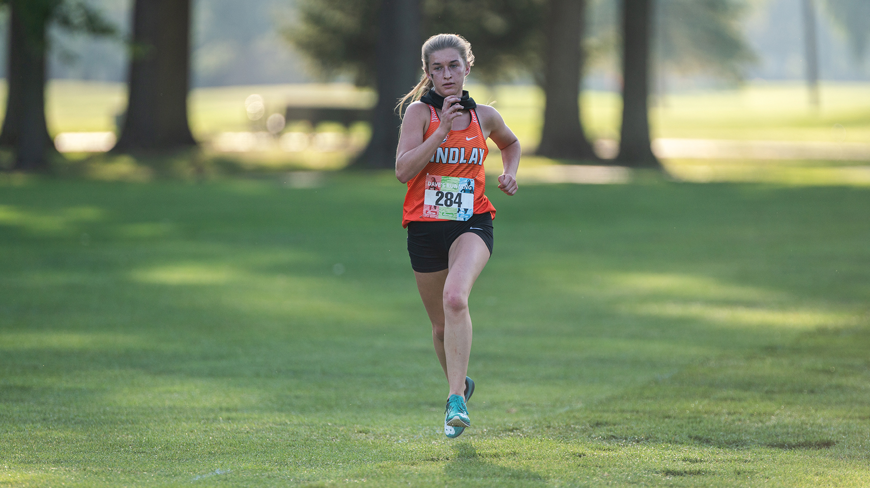 Women's cross country runner in orange racing through the shadows