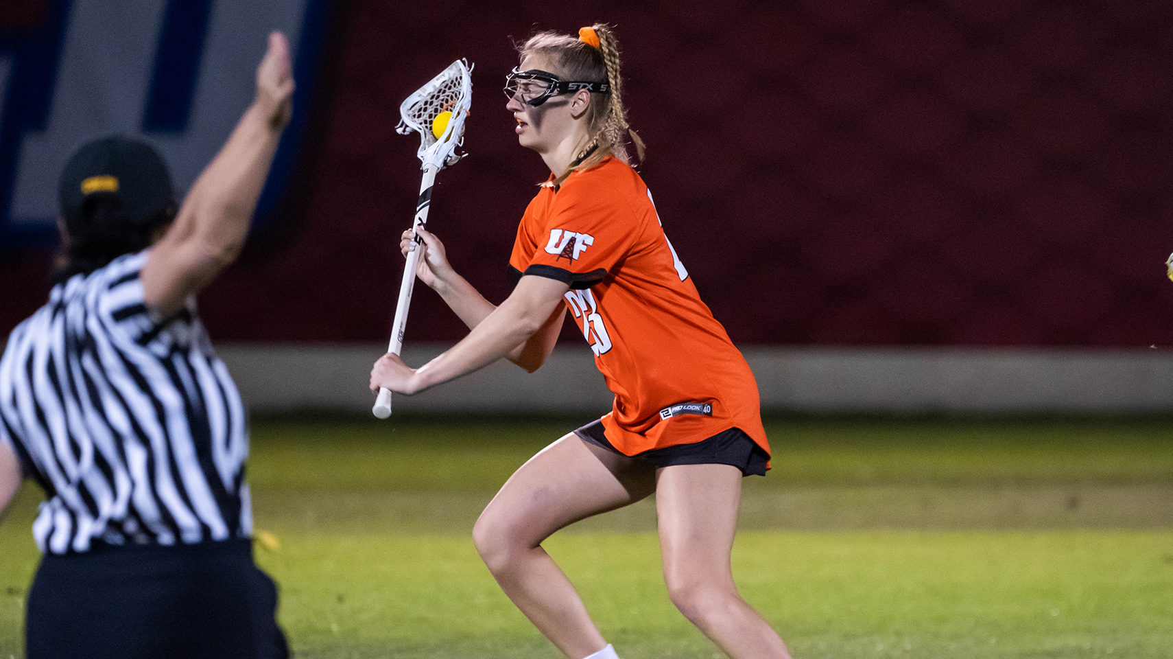 Women's lacrosse player in orange holding the ball in the middle of the field.